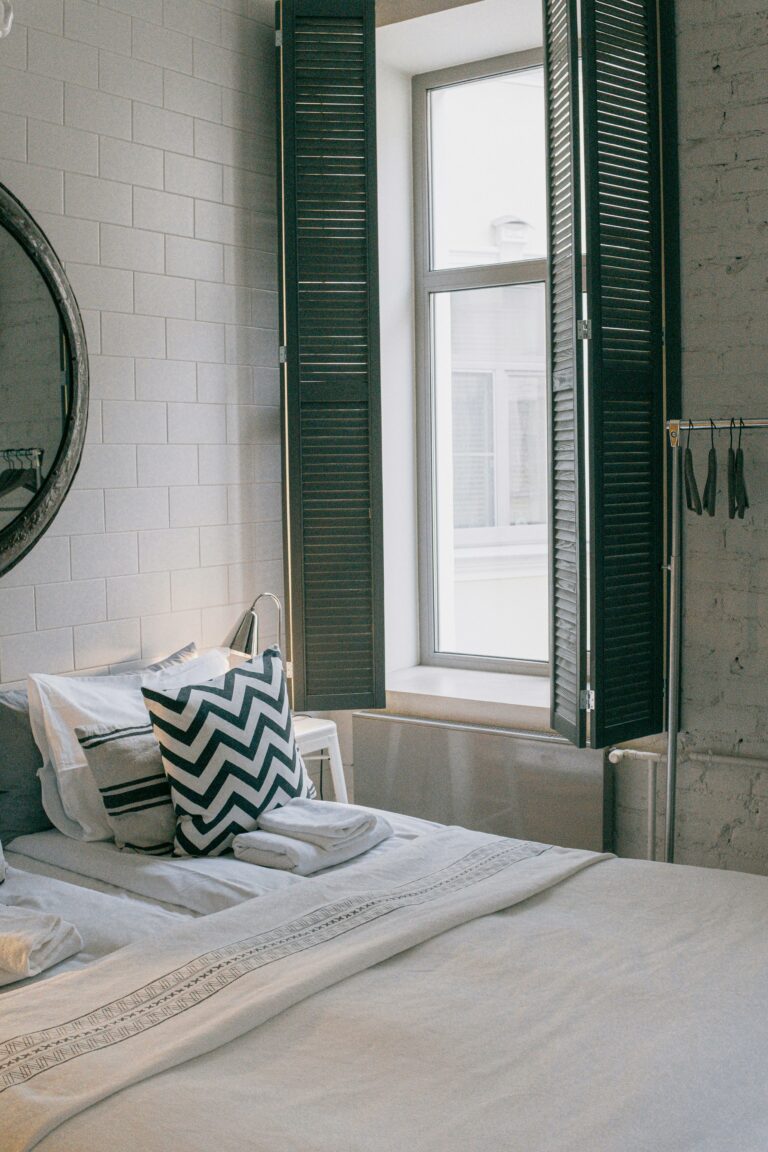 A cozy and stylish bedroom featuring modern decor and a sunlit window with shutter panels.